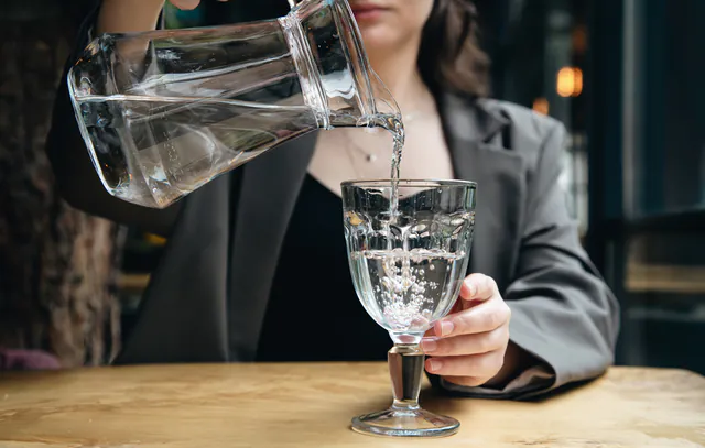 Close-up, a woman pours water into a glass in a cafe.