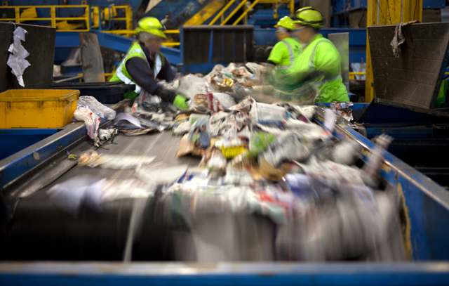 Workers separating paper and plastic on a conveyor belt in a recycling facility