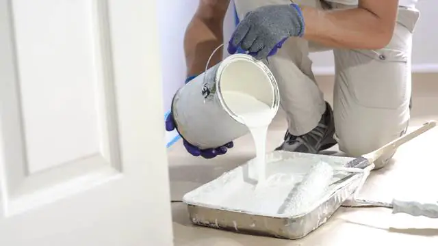 Professional interior construction worker pouring white color paint to tray.