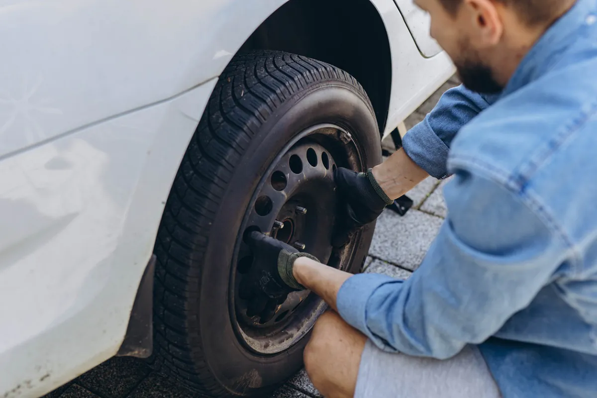 Young man in unscrewing lug nuts on car wheel in process of new tire replacement,using wrench while changing flat tire on the road.