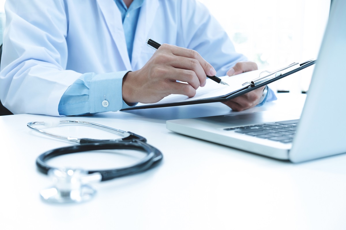 Doctor working with laptop computer and writing on paperwork. Ho