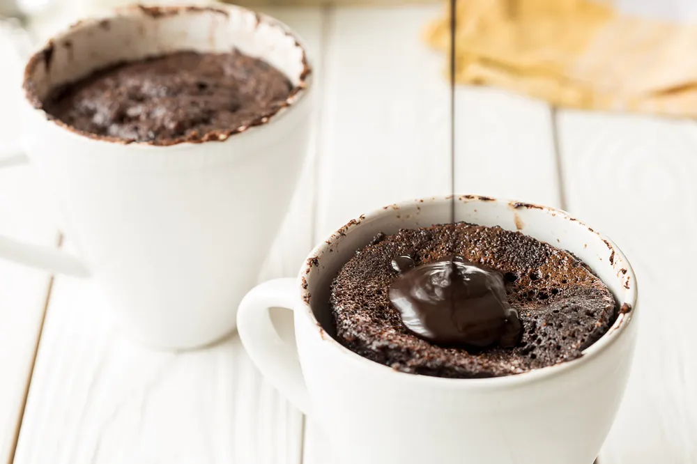 Pouring Chocolate Sauce on Chocolate Mug Cakes, Cupcakes on Light White Background